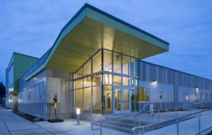 Exterior shot of the front door of Vanessa Behan. The building is grey and green, with a handprint logo on the glass of the entryway.