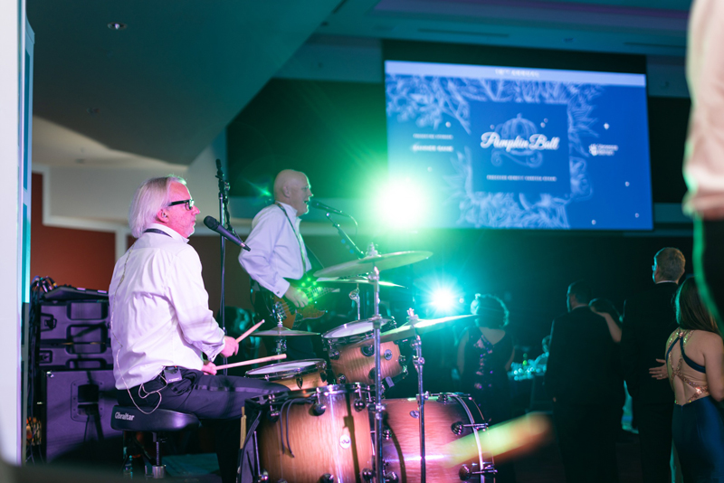 A live swing band plays on the venue's stage while the pumpkin ball brand design decorates the backdrop