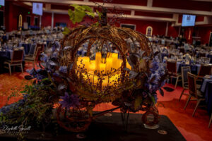 Pumpkin chariot decoration with candles on a table. The dining area of the venue is in the background.