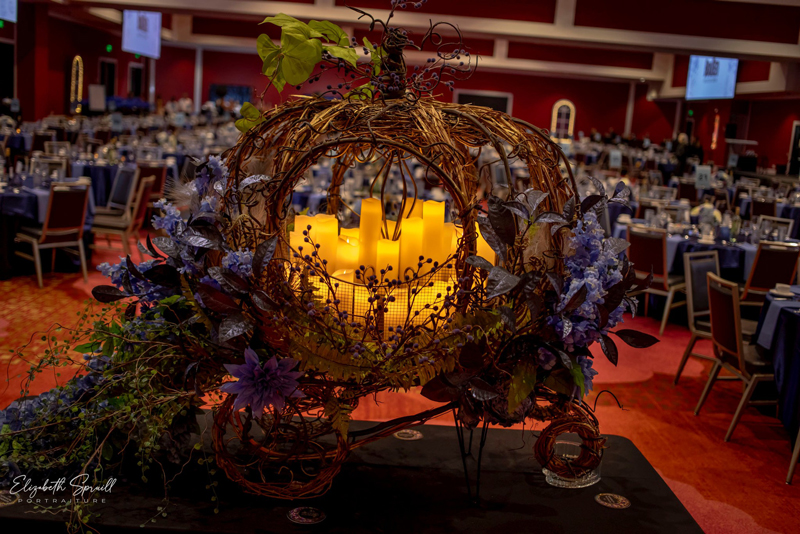 Pumpkin chariot decoration with candles on a table. The dining area of the venue is in the background.