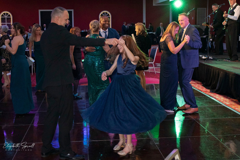 Two people dance in their black-tie attire on the dance floor as the live band plays in the background.